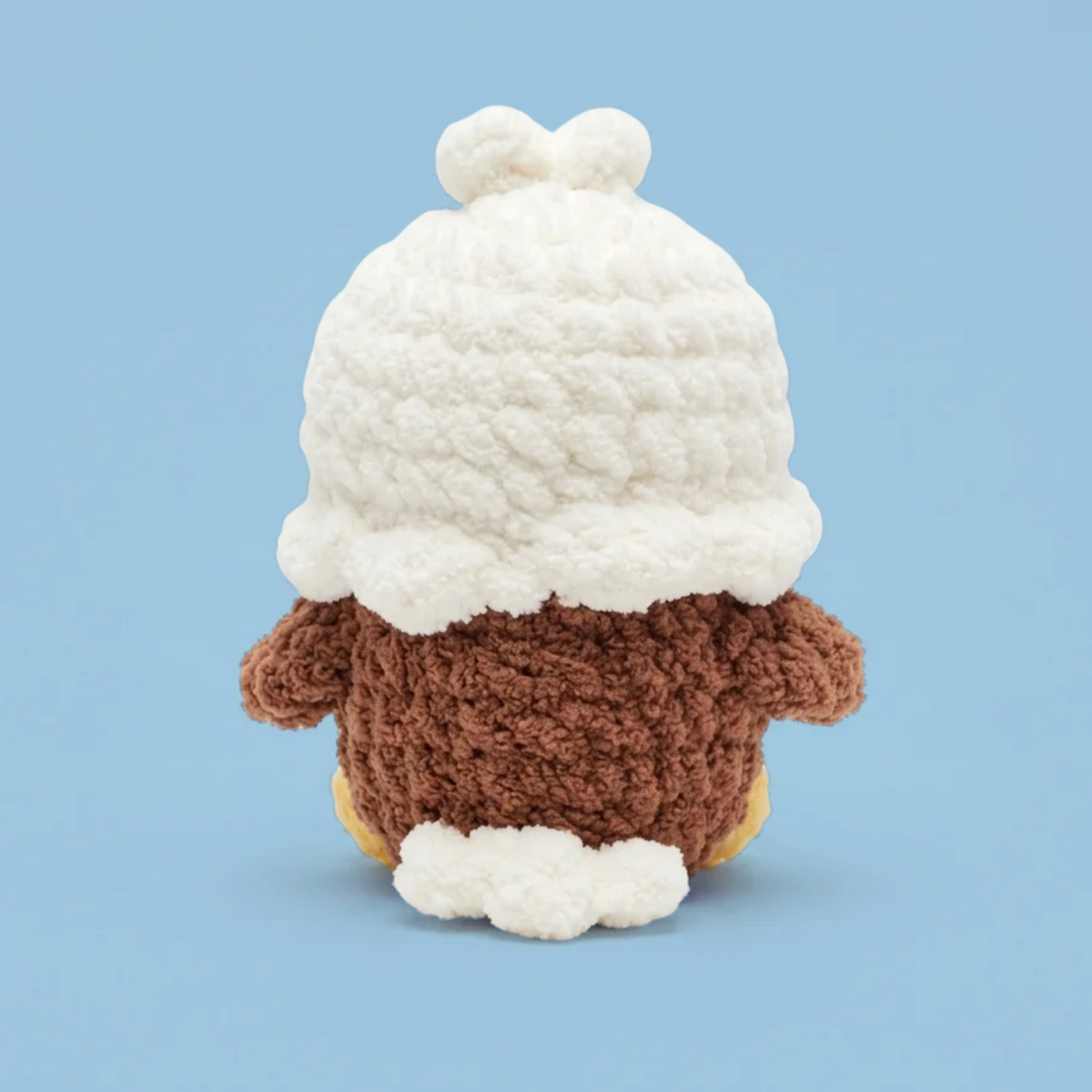 A crocheted plush toy shown from the back, featuring a brown textured body, a large white crocheted head, and small white crochet tail feathers at the bottom, set against a solid light blue background.